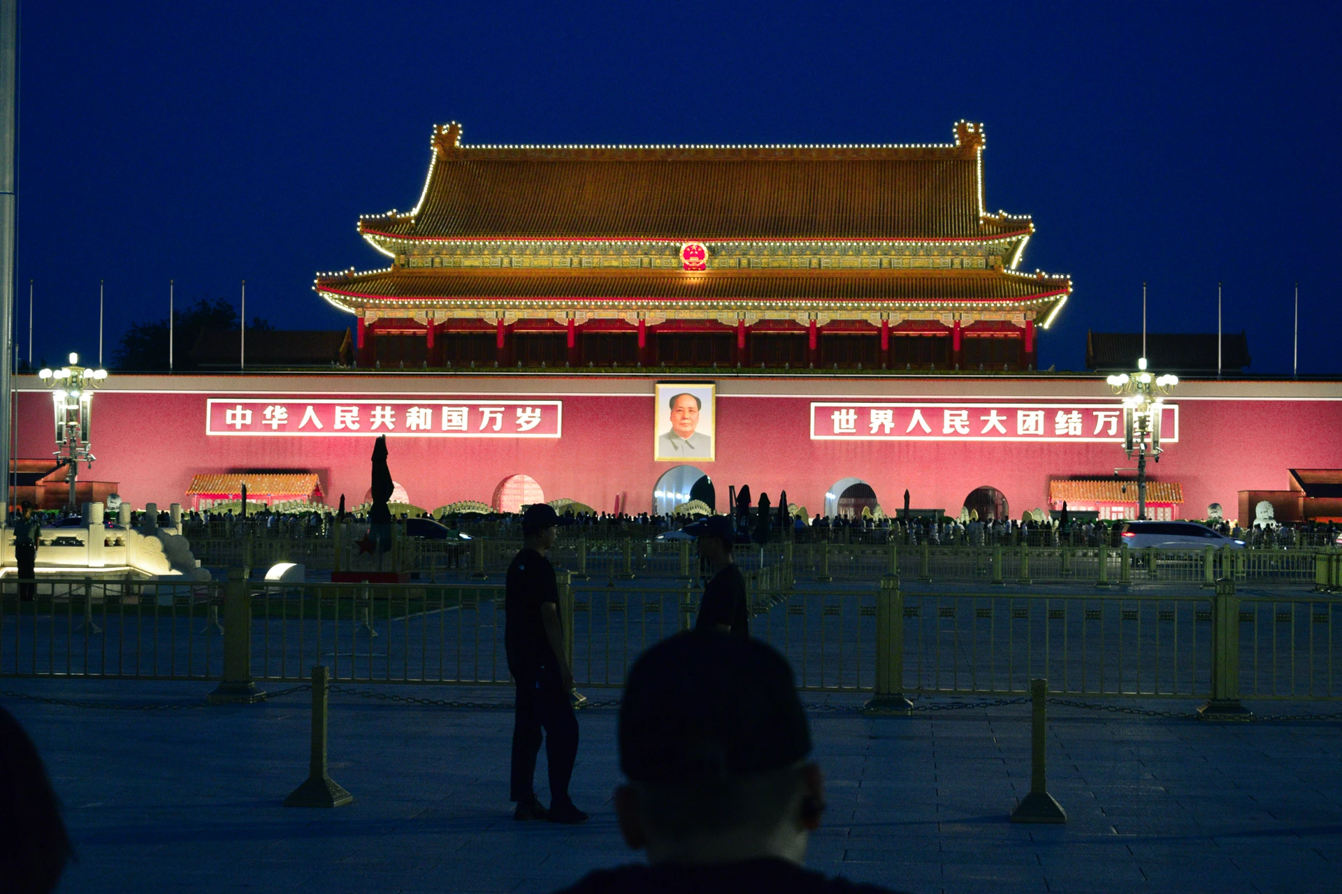 Visitors silhouetted in front of the illuminated Tiananmen gate at night