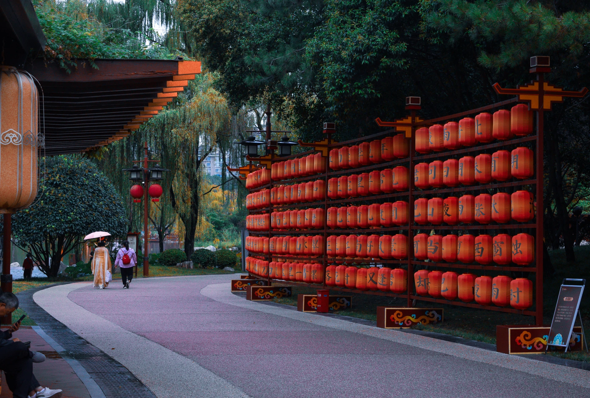 A wall of red lanterns beside a tree-lined walkway