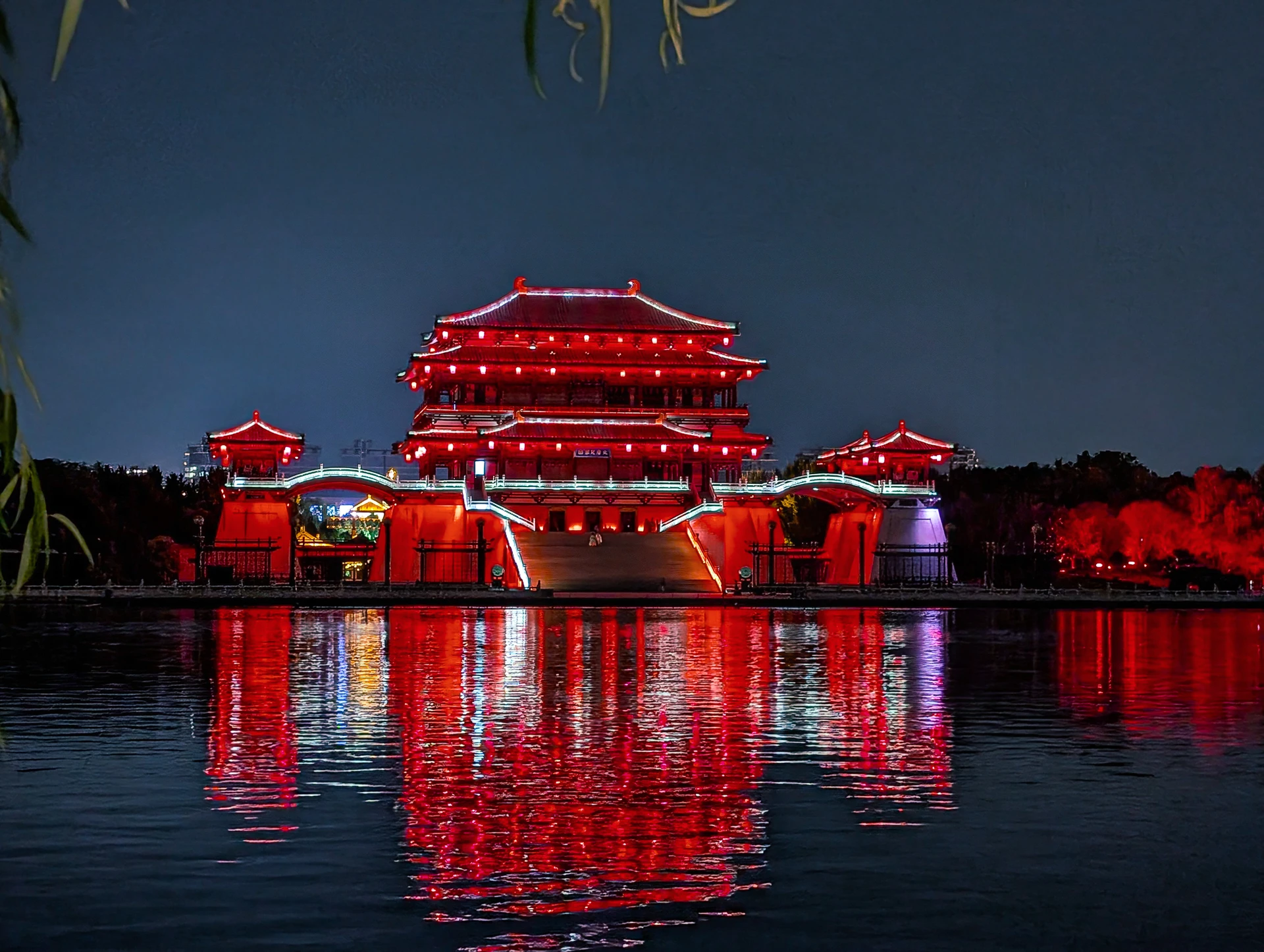 A red-lit pavilion and its reflection across a still lake at night