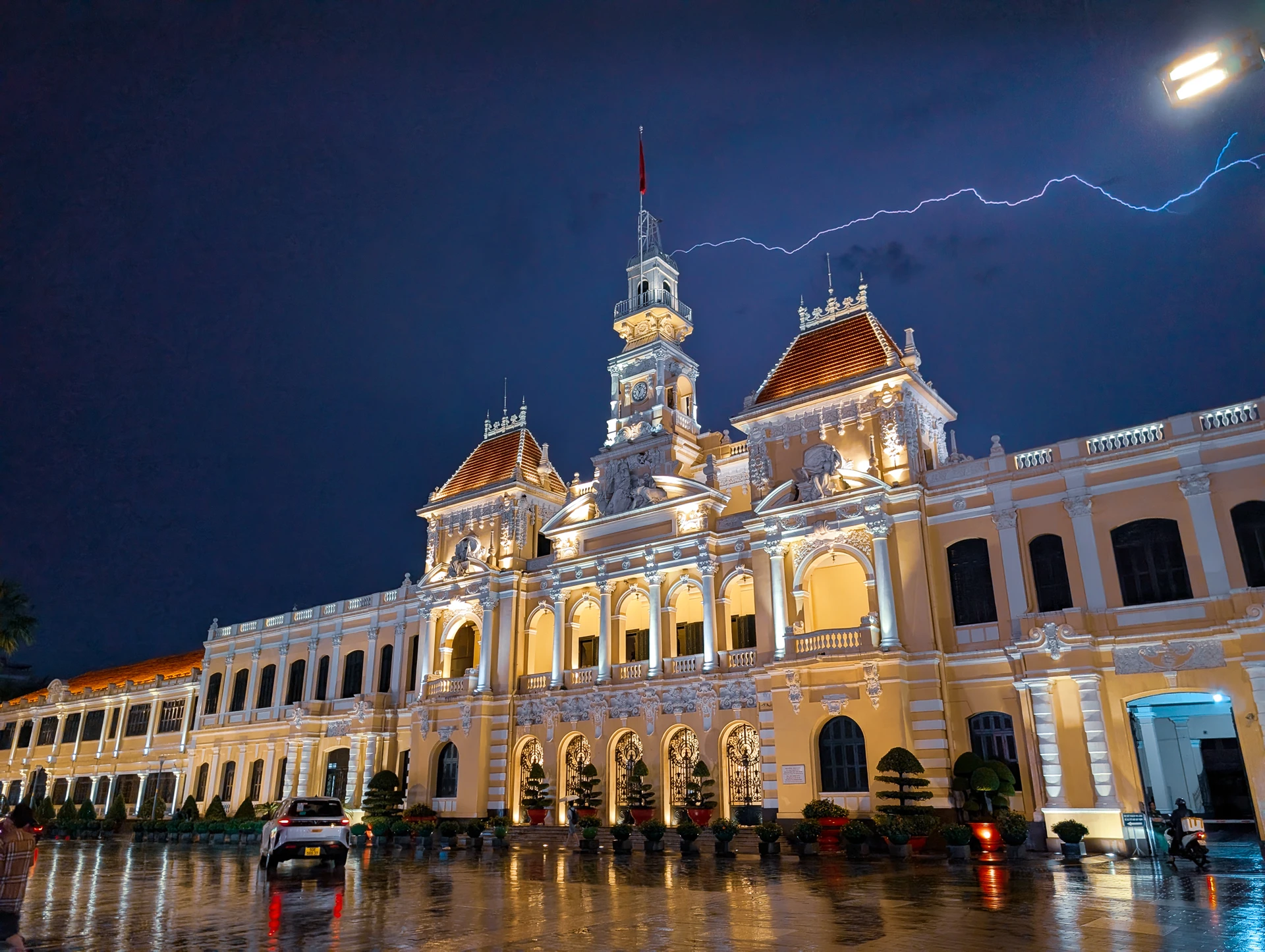 An ornate building illuminated in gold above a rain-soaked square at night