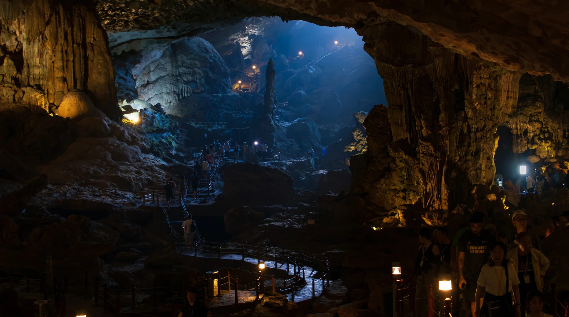 Visitors following a winding illuminated walkway through a cavern filled with blue light