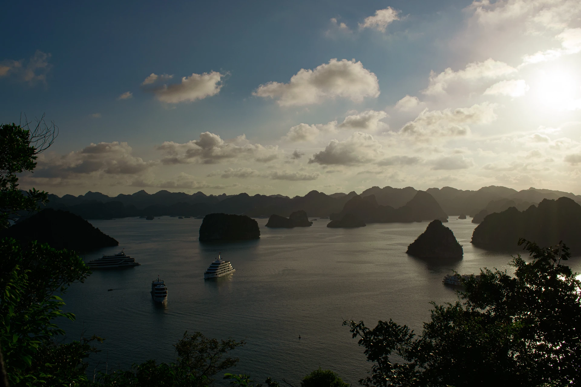 Boats moving between silhouetted limestone islands as low sunlight falls across the bay