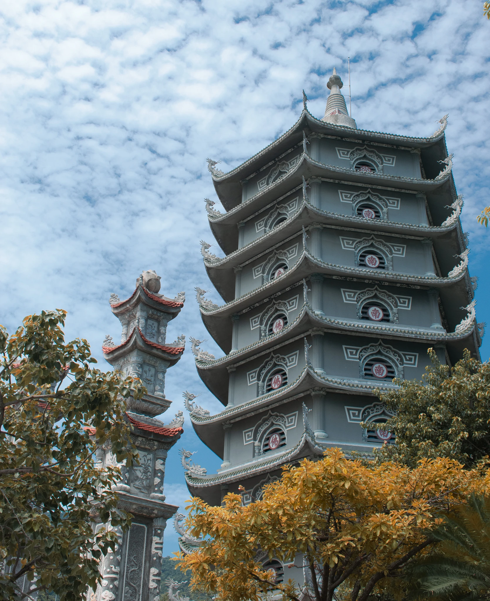 A tall pagoda with tiered roofs rising above trees beneath a sky of scattered white clouds
